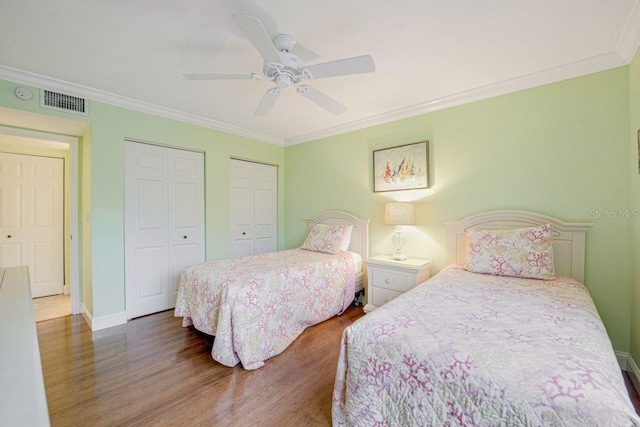 bedroom featuring baseboards, visible vents, ornamental molding, dark wood-type flooring, and multiple closets