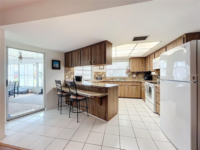 kitchen with ceiling fan, tasteful backsplash, kitchen peninsula, white appliances, and a breakfast bar area