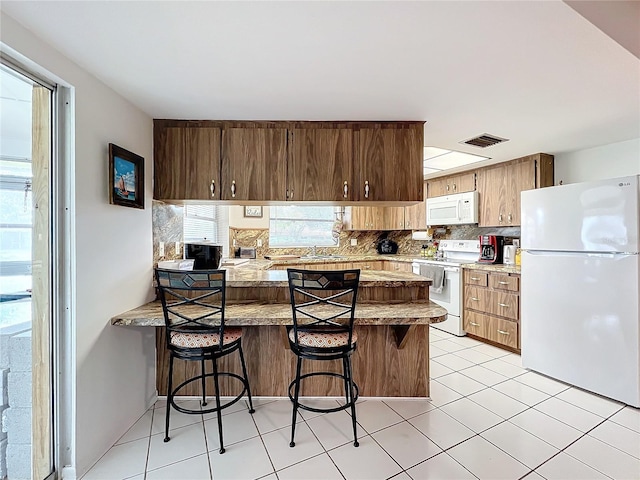 kitchen with tasteful backsplash, kitchen peninsula, white appliances, a breakfast bar area, and light tile patterned flooring