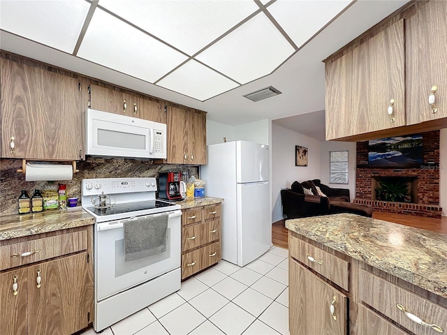 kitchen featuring backsplash, light tile patterned flooring, white appliances, and a brick fireplace