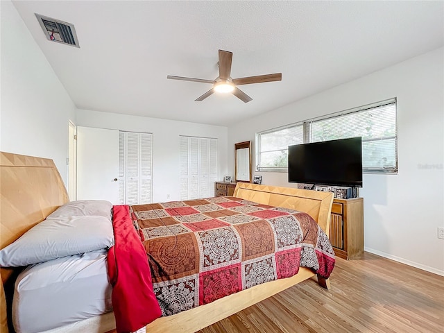 bedroom featuring multiple closets, ceiling fan, and hardwood / wood-style floors