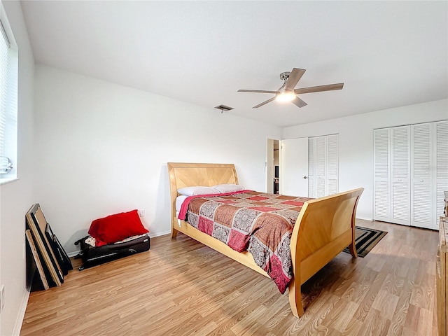 bedroom with ceiling fan, light hardwood / wood-style floors, and two closets