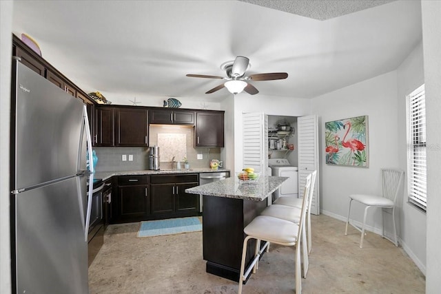 kitchen featuring a kitchen breakfast bar, decorative backsplash, light stone countertops, a kitchen island, and stainless steel appliances