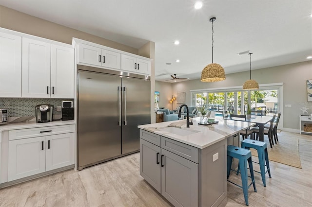 kitchen with ceiling fan, a center island with sink, stainless steel built in fridge, white cabinets, and hanging light fixtures