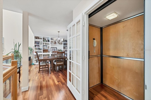 kitchen featuring elevator, built in features, hardwood / wood-style floors, pendant lighting, and a chandelier