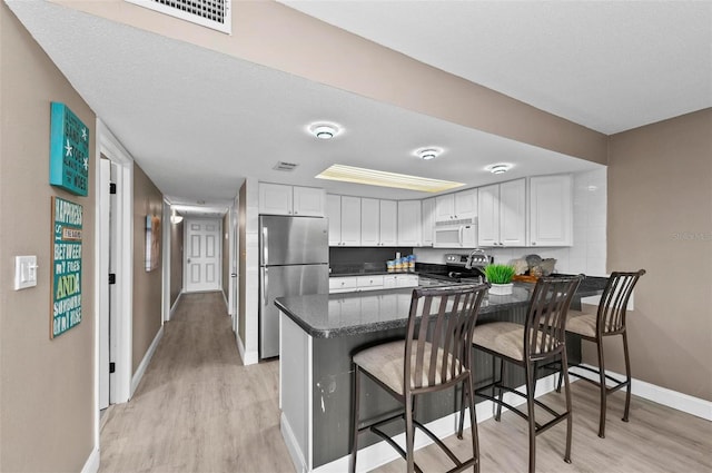 kitchen with kitchen peninsula, stainless steel appliances, light hardwood / wood-style flooring, white cabinetry, and a breakfast bar area