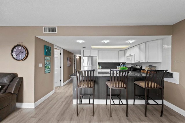 kitchen with a breakfast bar, kitchen peninsula, decorative backsplash, appliances with stainless steel finishes, and white cabinetry