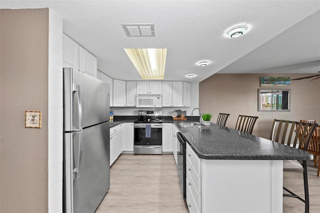 kitchen with kitchen peninsula, appliances with stainless steel finishes, a breakfast bar, and white cabinets