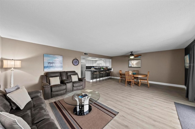 living room featuring ceiling fan, light wood-type flooring, and a textured ceiling