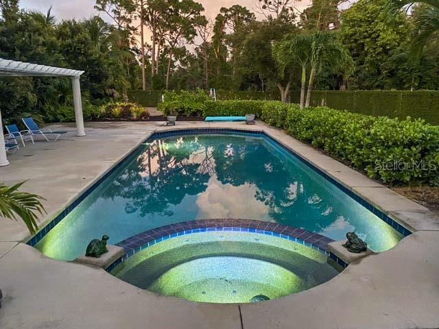 pool at dusk with an in ground hot tub and a patio