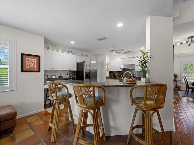 kitchen with a breakfast bar, backsplash, stainless steel fridge, white cabinetry, and kitchen peninsula