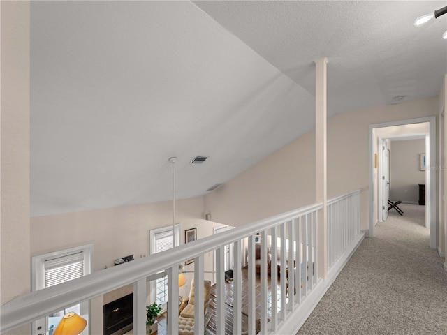 hall with a textured ceiling, light carpet, and lofted ceiling