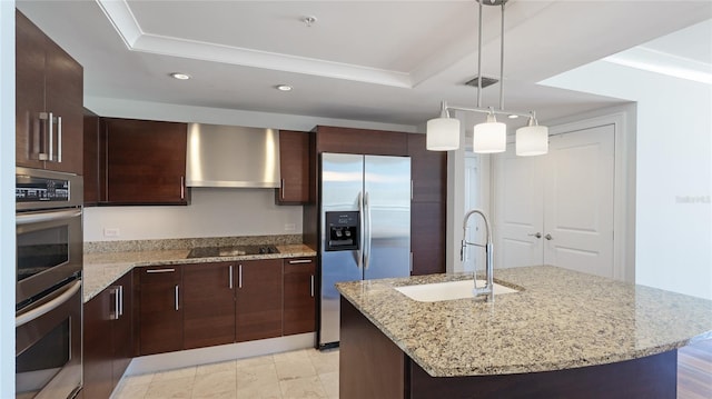 kitchen featuring appliances with stainless steel finishes, decorative light fixtures, sink, wall chimney range hood, and a center island with sink