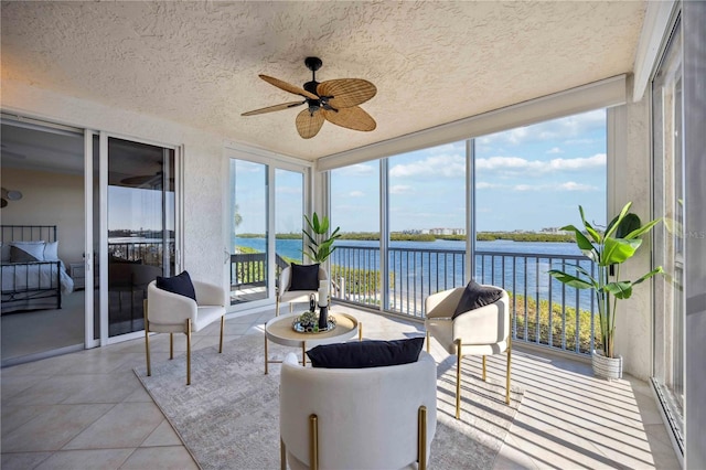 sunroom with ceiling fan and a water view