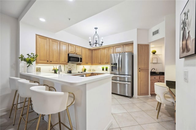 kitchen with light tile patterned floors, decorative light fixtures, a kitchen bar, kitchen peninsula, and stainless steel appliances