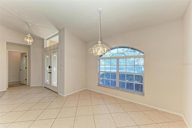 spare room featuring a notable chandelier, light tile patterned flooring, and a textured ceiling