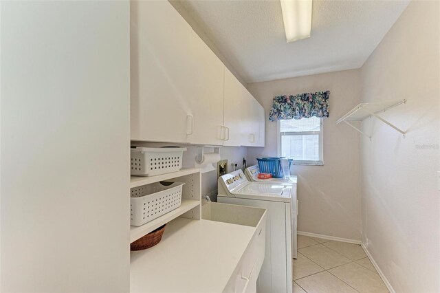 clothes washing area featuring washing machine and clothes dryer, light tile patterned flooring, and cabinets