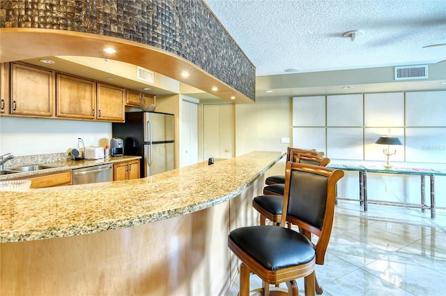 kitchen featuring a breakfast bar, a textured ceiling, stainless steel appliances, and sink