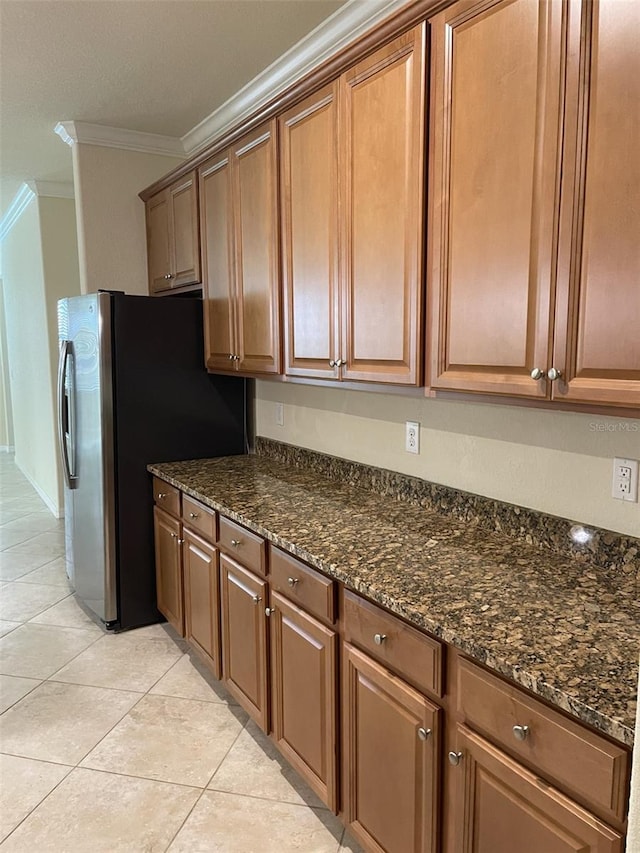 kitchen featuring light tile patterned flooring, dark stone countertops, ornamental molding, and stainless steel refrigerator