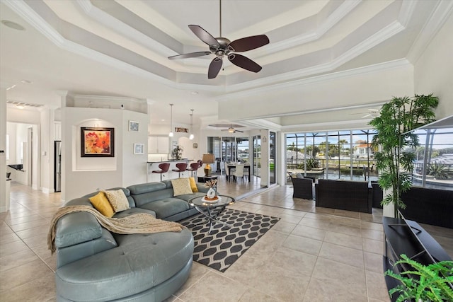 tiled living room with a tray ceiling, ceiling fan, crown molding, and a high ceiling