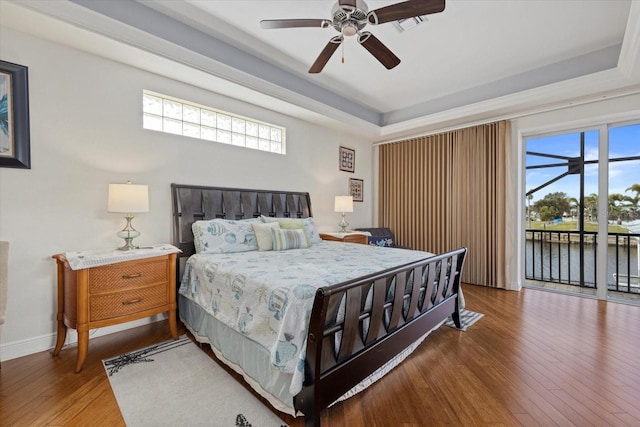 bedroom featuring a tray ceiling, multiple windows, ceiling fan, and a water view