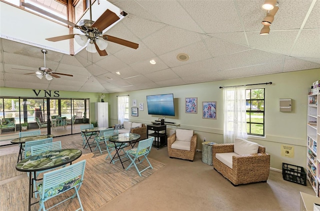 carpeted living room featuring ceiling fan, a drop ceiling, and a healthy amount of sunlight