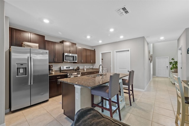 kitchen with sink, a breakfast bar, a kitchen island with sink, appliances with stainless steel finishes, and dark brown cabinetry