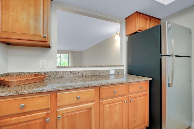 kitchen featuring lofted ceiling, stainless steel fridge, and light stone counters