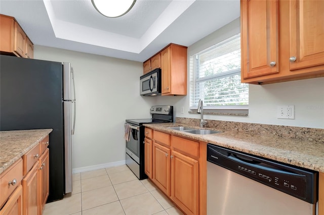 kitchen featuring a raised ceiling, sink, light stone countertops, appliances with stainless steel finishes, and light tile patterned floors