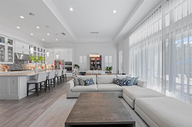 living room with ornamental molding, light wood-type flooring, and a tray ceiling