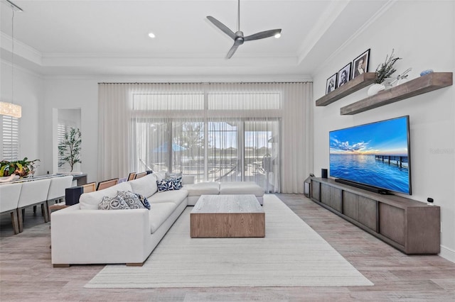 living room featuring crown molding, ceiling fan, a tray ceiling, and light hardwood / wood-style flooring