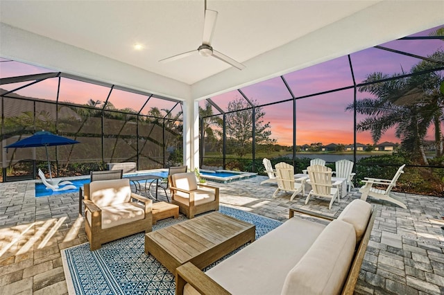 patio terrace at dusk featuring an outdoor hangout area, glass enclosure, ceiling fan, and an in ground hot tub