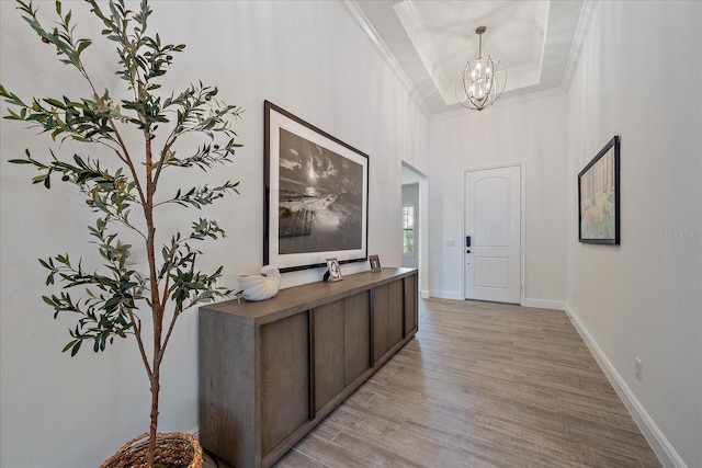 entryway with a notable chandelier, baseboards, light wood finished floors, a raised ceiling, and crown molding