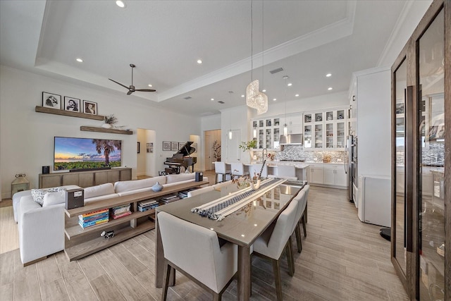 dining room with light wood finished floors, a tray ceiling, and ornamental molding