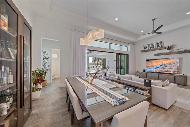 dining space featuring light wood-type flooring, a raised ceiling, crown molding, and baseboards