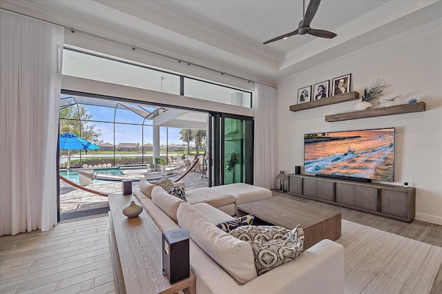 living room featuring light wood finished floors, a raised ceiling, a sunroom, ceiling fan, and crown molding