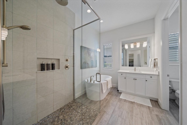 bathroom featuring a freestanding tub, toilet, wood finished floors, vanity, and tiled shower