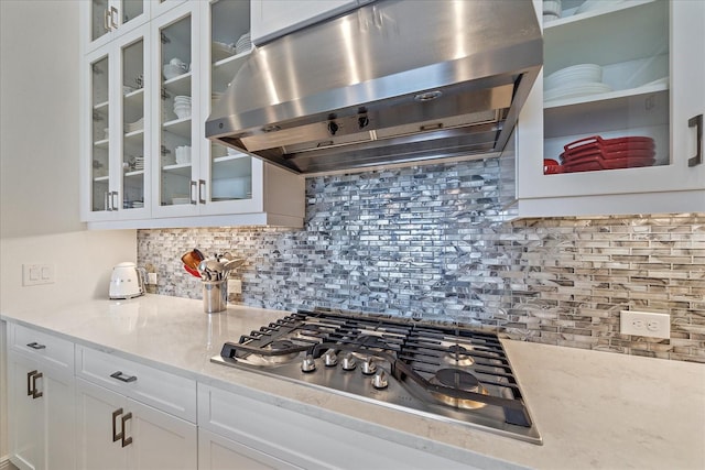 kitchen with decorative backsplash, stainless steel gas cooktop, glass insert cabinets, extractor fan, and white cabinetry