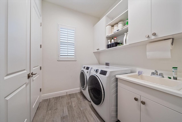 clothes washing area with a sink, baseboards, cabinet space, light wood finished floors, and washer and clothes dryer