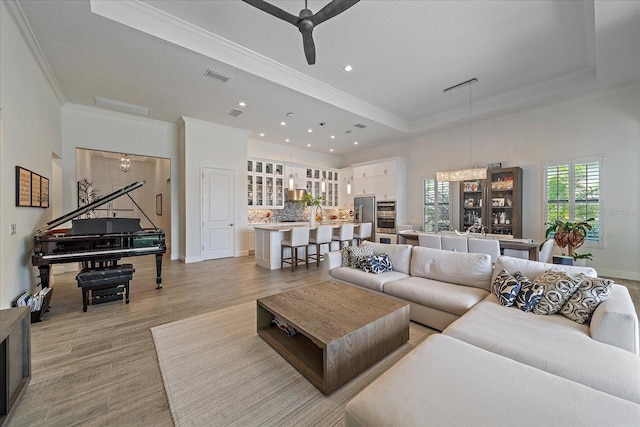 living area with visible vents, baseboards, ornamental molding, light wood finished floors, and a raised ceiling