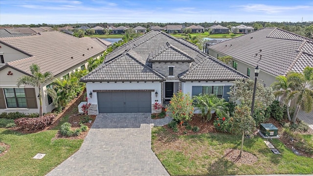 view of front of property with decorative driveway, a garage, a residential view, stone siding, and a tiled roof