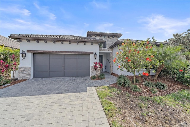 mediterranean / spanish house featuring a garage, a tiled roof, decorative driveway, and stucco siding