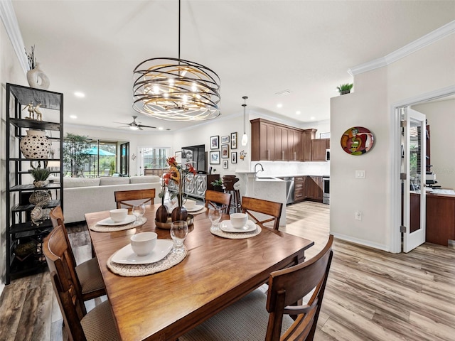 dining area with crown molding, light hardwood / wood-style floors, ceiling fan with notable chandelier, and sink