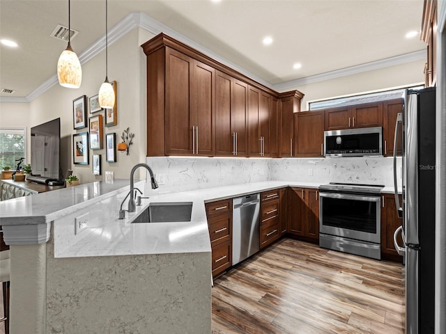 kitchen featuring kitchen peninsula, appliances with stainless steel finishes, decorative light fixtures, light stone countertops, and sink