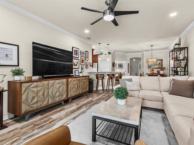 living room with ceiling fan with notable chandelier, ornamental molding, and light hardwood / wood-style floors