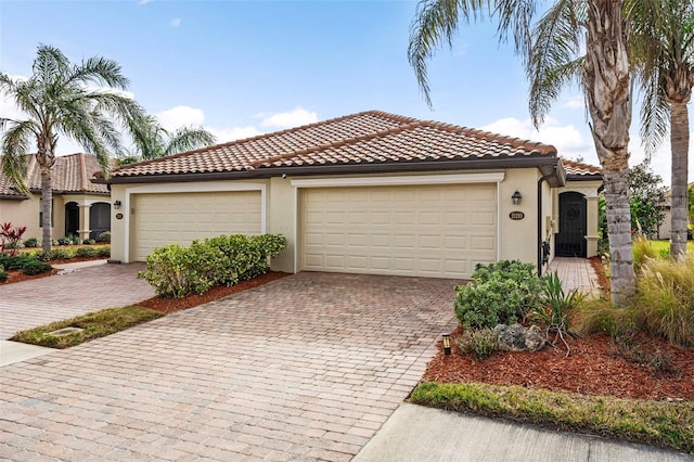 mediterranean / spanish house with stucco siding, a tiled roof, decorative driveway, and an attached garage