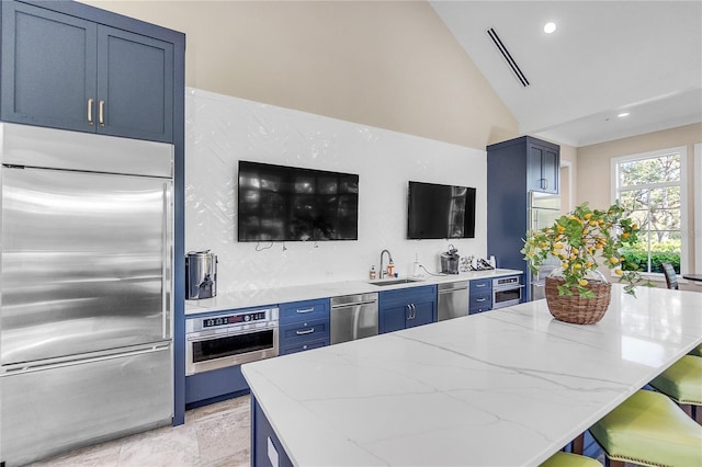 kitchen featuring lofted ceiling, sink, blue cabinetry, light stone counters, and stainless steel appliances