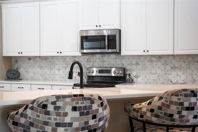 kitchen with backsplash, white cabinets, a breakfast bar area, and appliances with stainless steel finishes