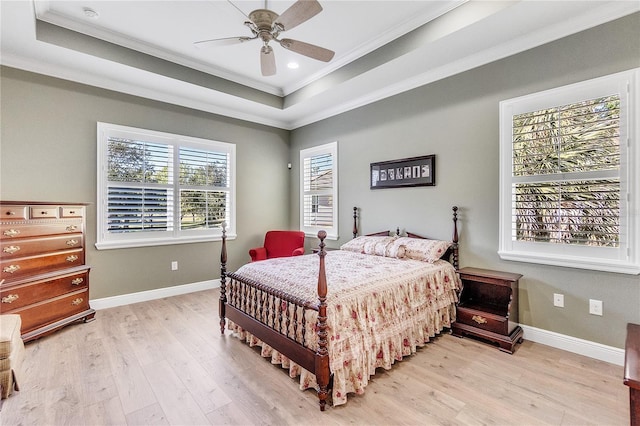 bedroom featuring ceiling fan, a raised ceiling, light wood-type flooring, and crown molding