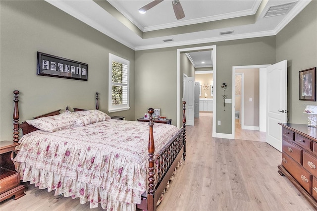 bedroom featuring light wood-type flooring, ensuite bath, a raised ceiling, ceiling fan, and crown molding